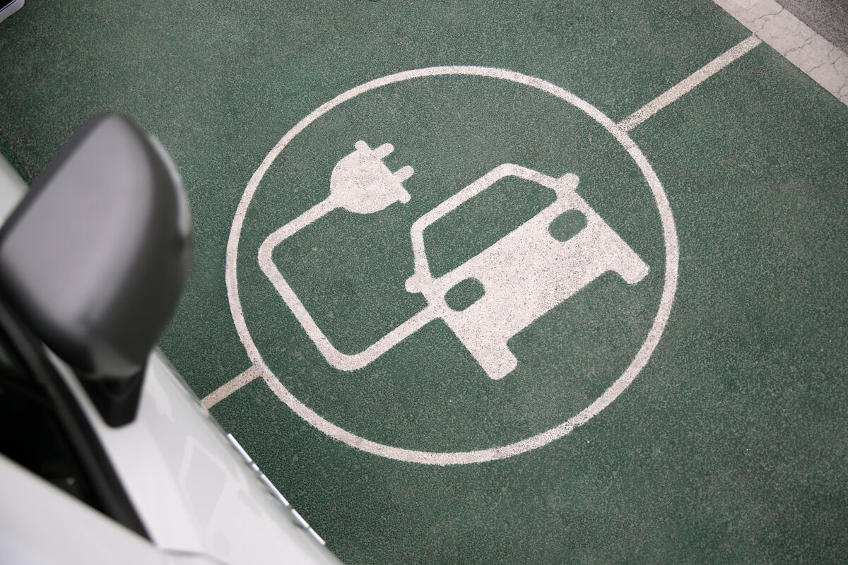 Un'auto elettrica in fase di ricarica, con il simbolo di ricarica disegnato sull'asfalto, che rappresenta la mobilità sostenibile