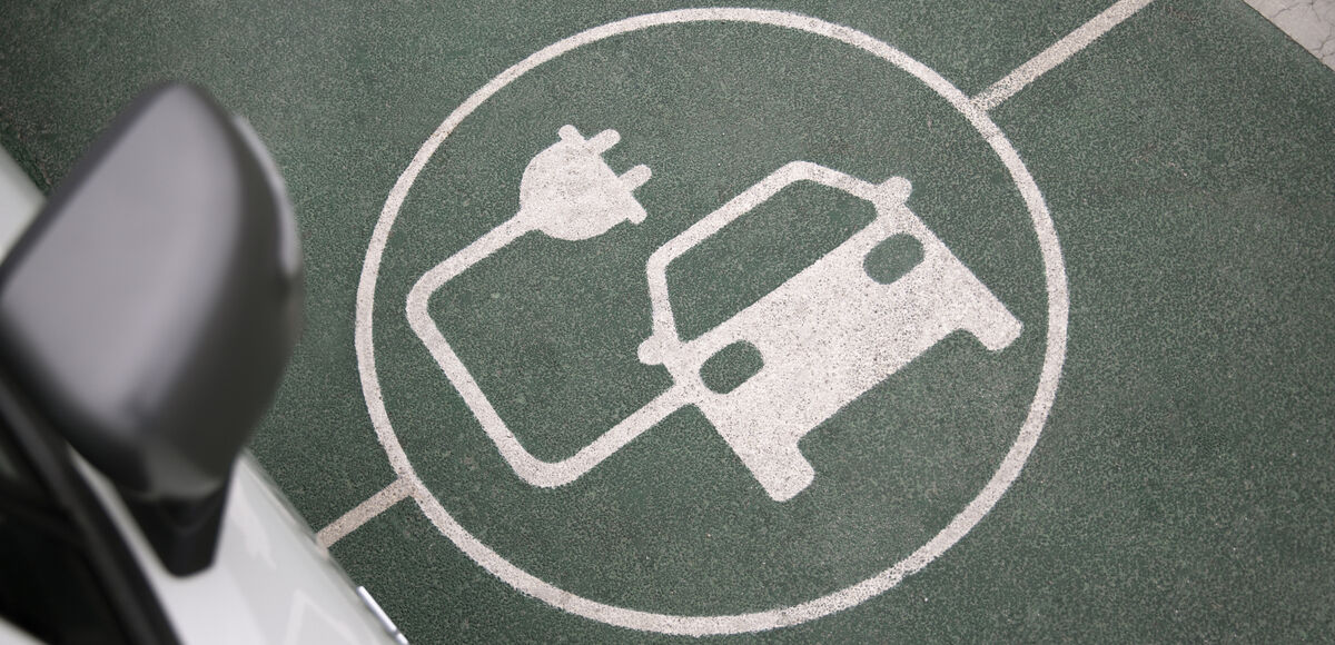 Un'auto elettrica in fase di ricarica, con il simbolo di ricarica disegnato sull'asfalto, che rappresenta la mobilità sostenibile