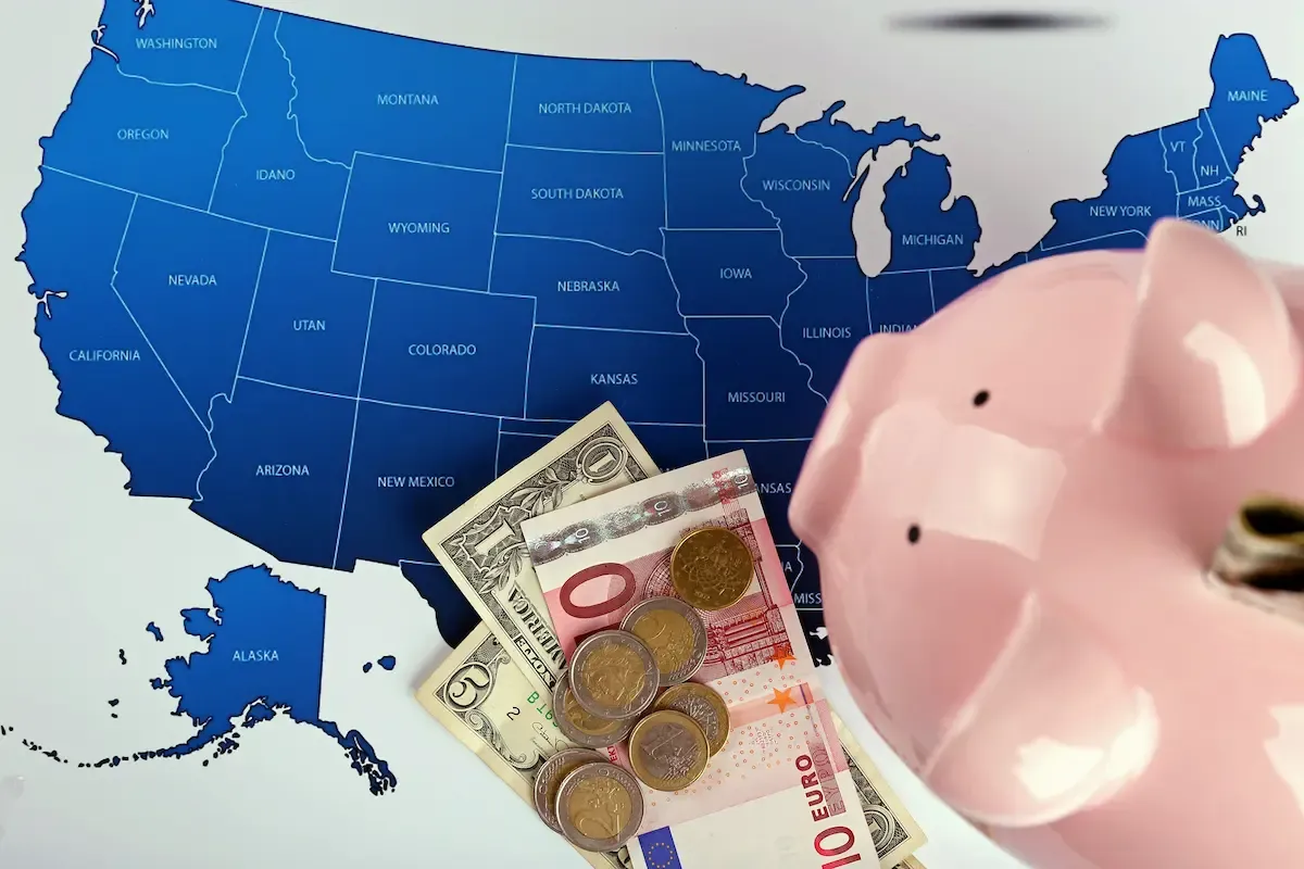 Mappa degli Stati Uniti con Euro e Dollari e un salvadanaio in primo piano, a rappresentare la tassazione statale e i redditi esteri in America.
