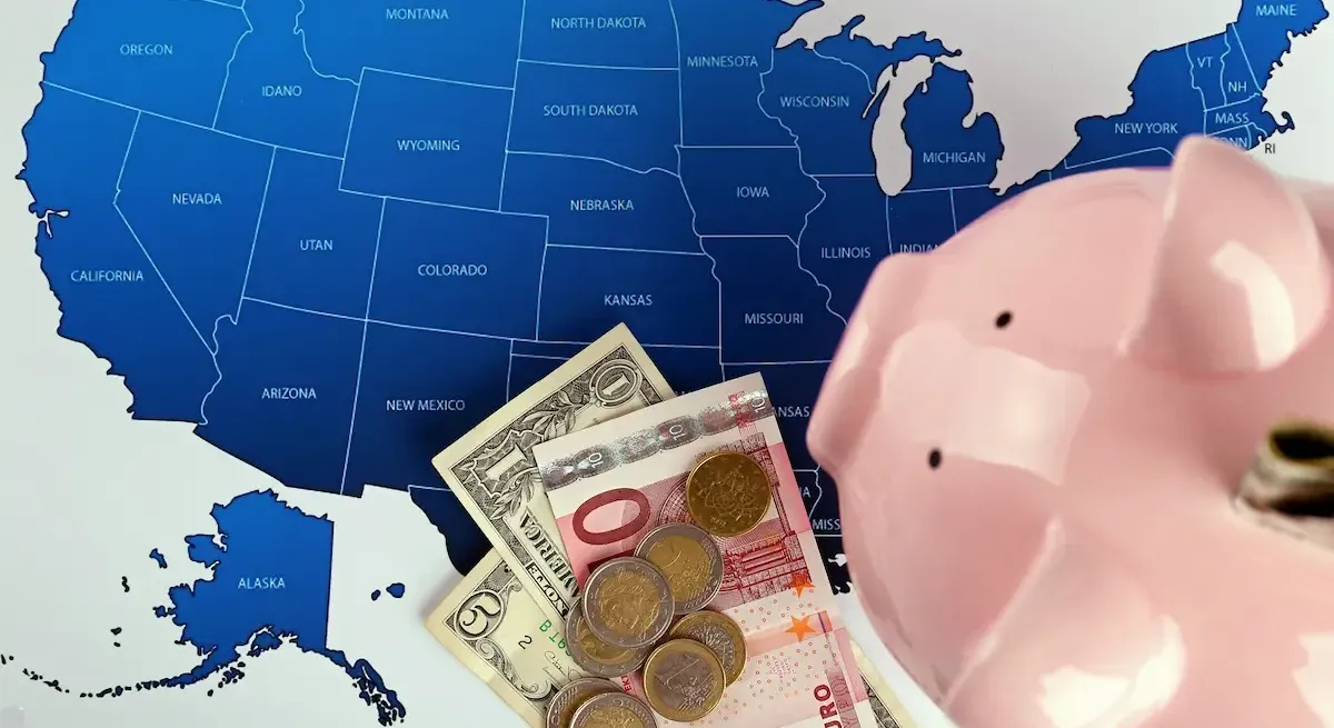 Mappa degli Stati Uniti con Euro e Dollari e un salvadanaio in primo piano, a rappresentare la tassazione statale e i redditi esteri in America.