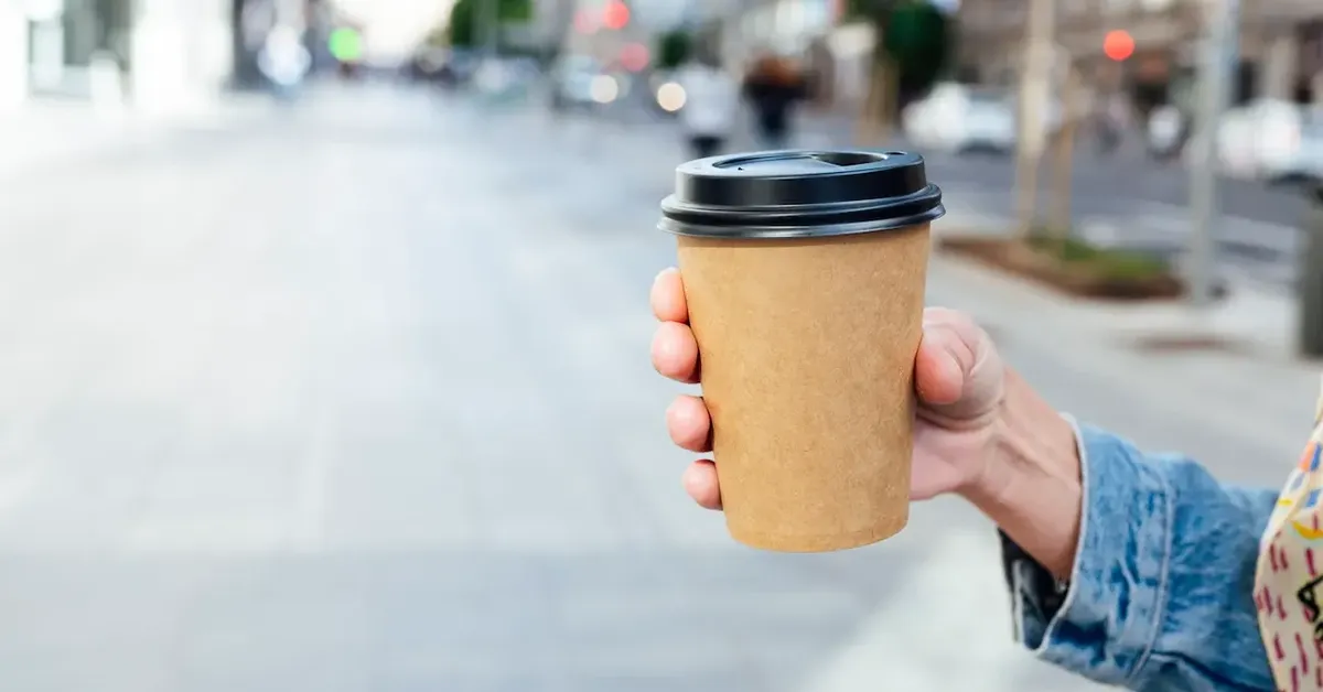 Mano che tiene una tazza di caffè da asporto, simboleggiando la convenienza dei punti vendita intelligenti Amazon Go e Starbucks a New York