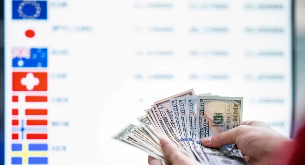 Mani che contano dollari USA di fronte a un tabellone di cambio valuta internazionale, simboleggiando i finanziamenti SACE SIMEST per l'export