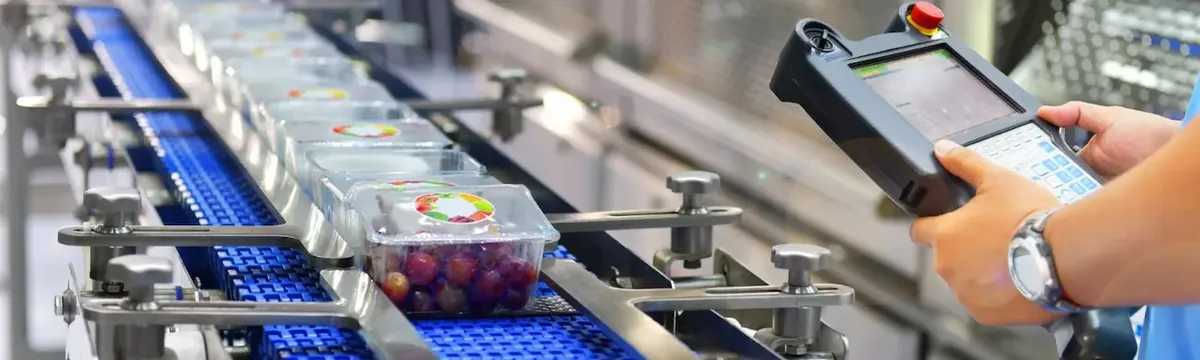Linea di confezionamento industriale con operatore e prodotti alimentari freschi, che simboleggia il processo di produzione e controllo qualità.