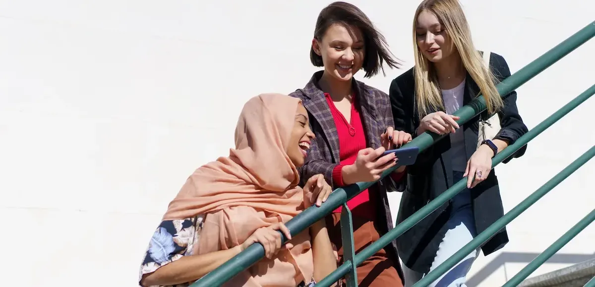 Gruppo di amici che interagiscono e condividono uno smartphone, inclusa una persona con hijab