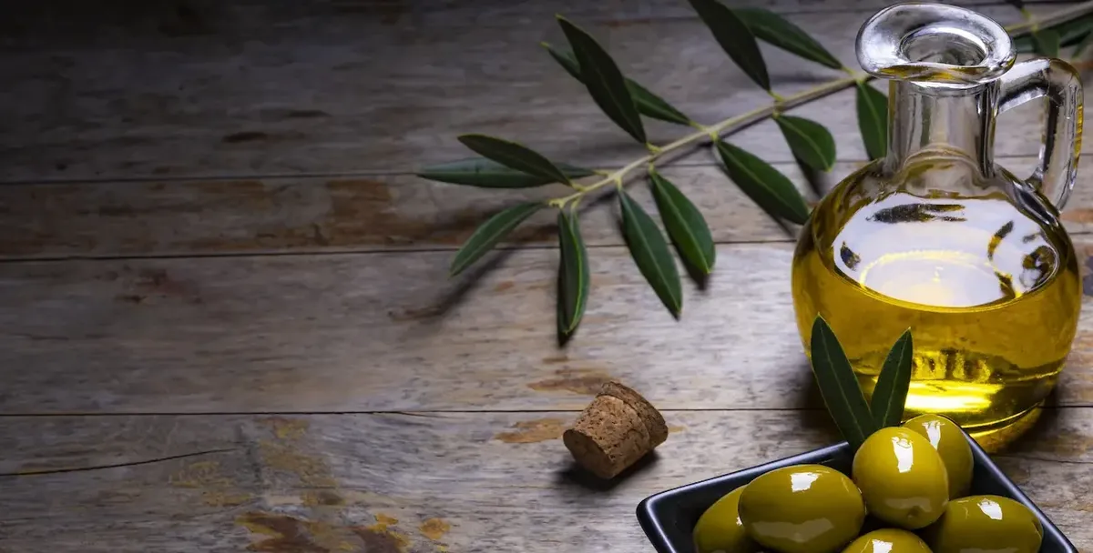 Bottiglia di olio extra vergine d'oliva con olive verdi e ramoscello d'ulivo su fondo di legno, evocando qualità e autenticità del prodotto