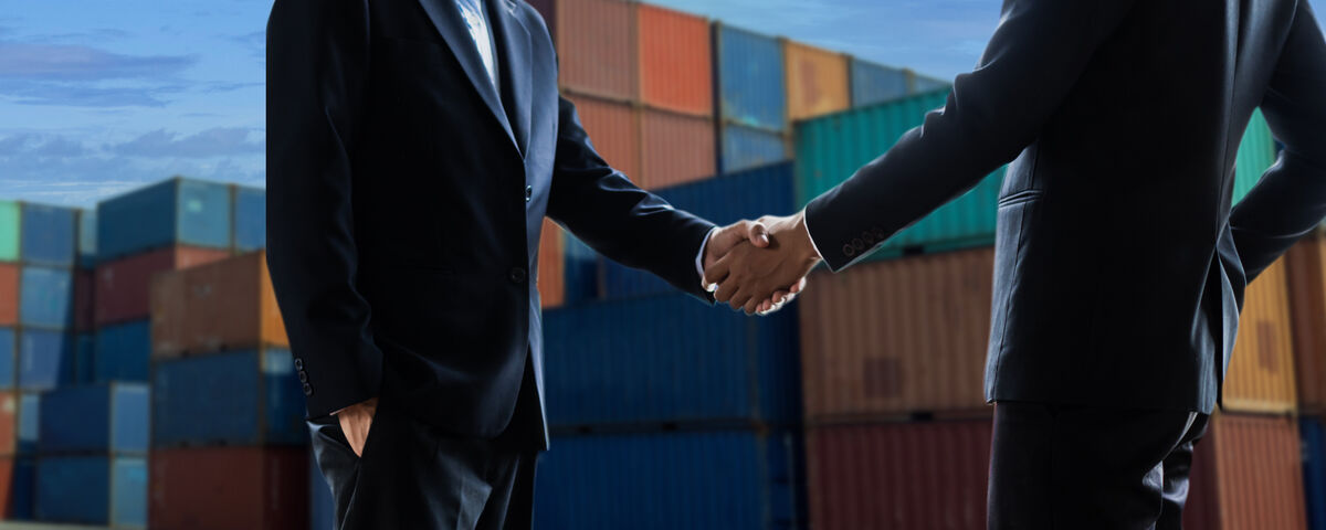 Stretta di mano tra professionisti con container sullo sfondo, simboleggiante accordi e logistica per l'export internazionale