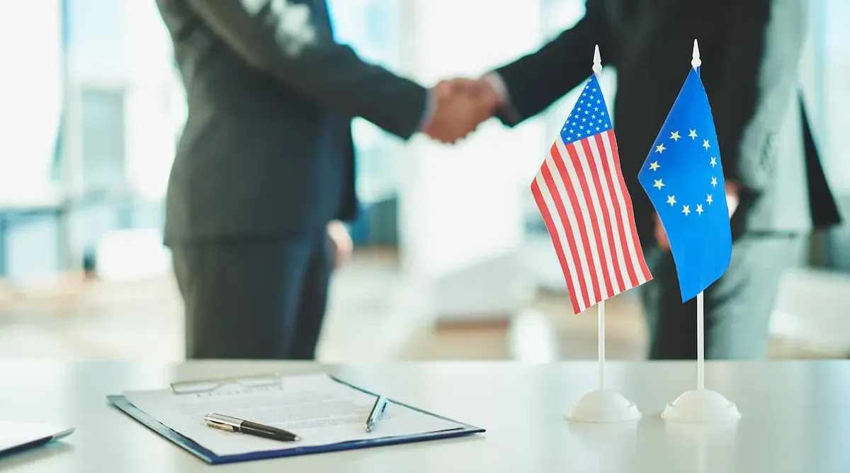 Primo piano di una stretta di mano tra uomini d'affari, con bandiere USA ed UE, che simboleggia accordi e finanziamenti internazionali