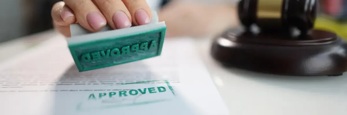 Mano che appone un timbro 'APPROVED' su un documento di certificazione