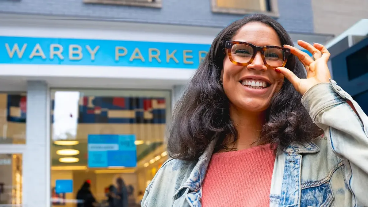 Cliente felice davanti a un negozio Warby Parker, che rappresenta la combinazione di e-commerce e retail fisico del marchio