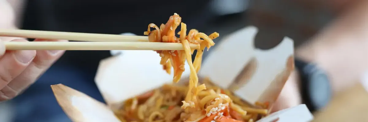 Primo piano di noodles da asporto di alta qualità in un contenitore di cartone, simbolo dei pasti genuini consegnati in ufficio a San Francisco e New York