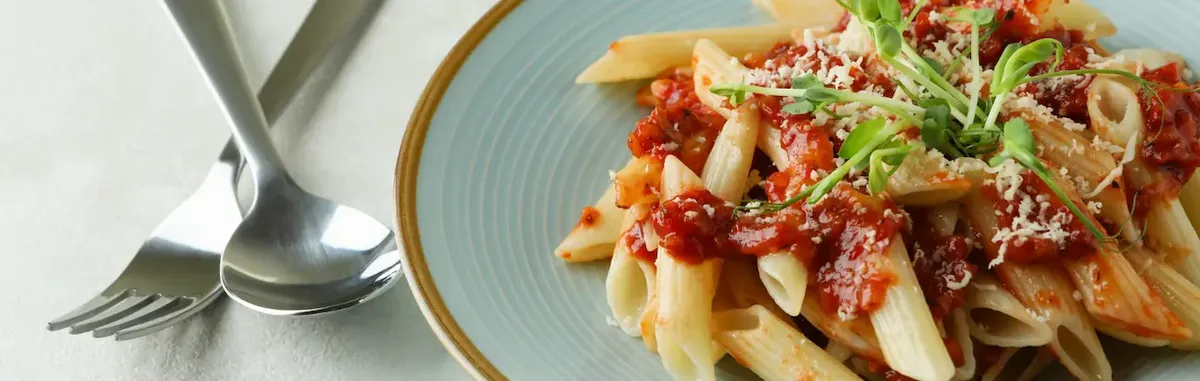 Piatto di penne con sugo al pomodoro e formaggio grattugiato, con decorazione di germogli