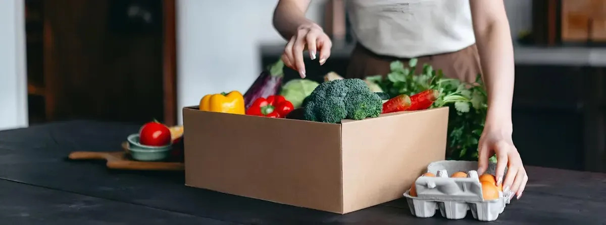 Persona che prepara un pasto in una cucina moderna con verdure fresche e uova, a simboleggiare le nuove tendenze alimentari e i meal kit
