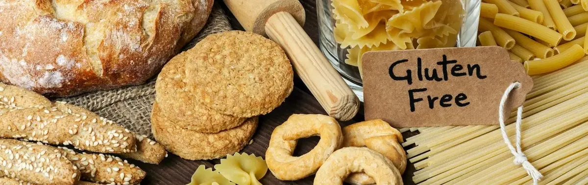 Vasta selezione di prodotti senza glutine su una tavola rustica, inclusi pane, biscotti e pasta, con un cartellino 'Gluten Free' in evidenza