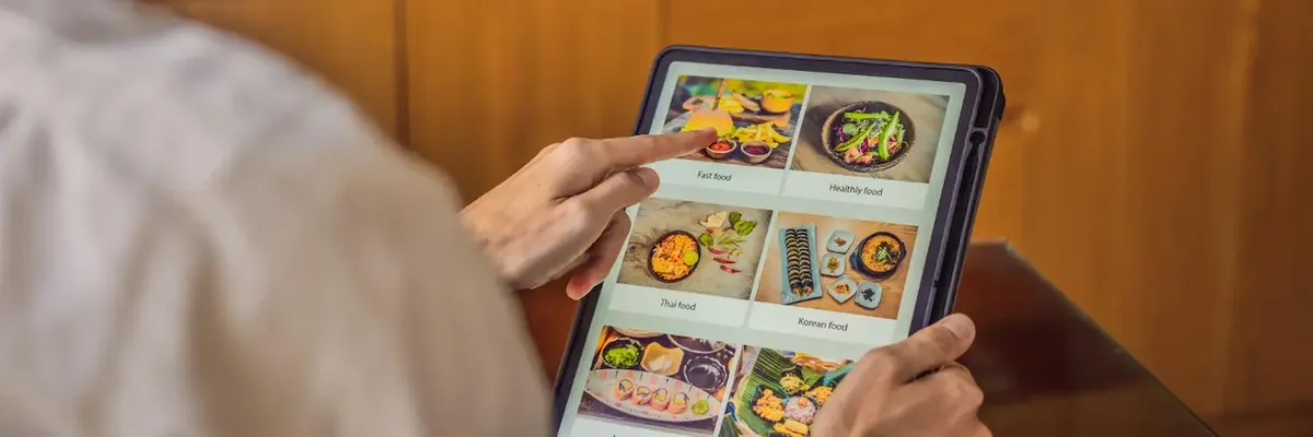 Persona con tablet mostra vari piatti (fast food, sano, thai), simboleggiando le tendenze della ristorazione