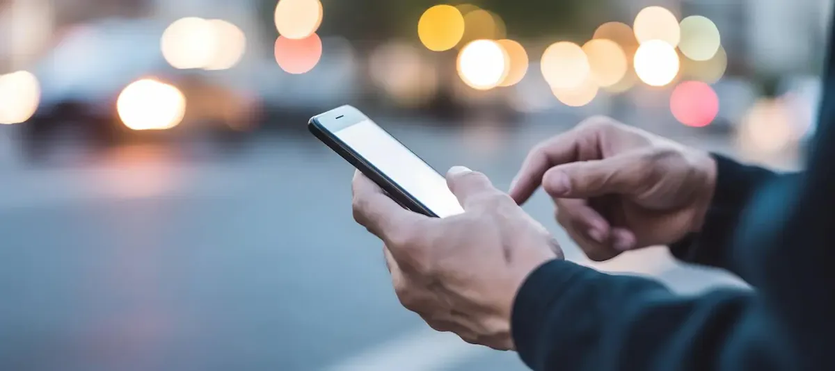 Mani che tengono smartphone, sullo sfondo luci sfocate di una città, simbolo di tecnologia e navigazione mobile
