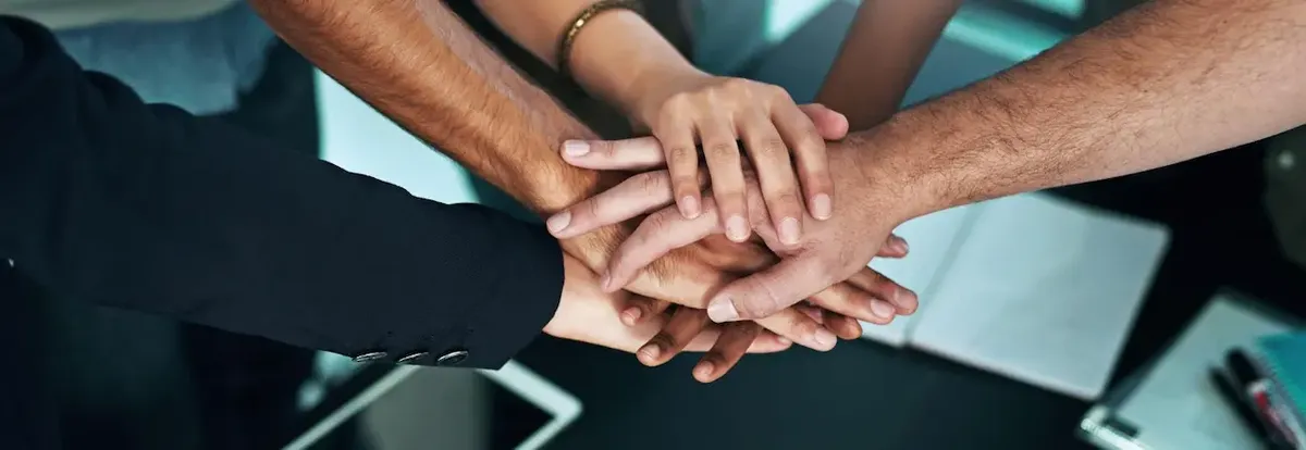 Mani di sei persone diverse sovrapposte sul tavolo, simboleggiando il crowdfunding e l'unione per l'avvio di un ristorante.