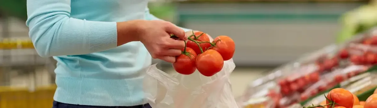 Persona che seleziona con cura pomodori freschi in un supermercato, simboleggiando la crescente attenzione dei consumatori (Millennials/Teenager) per la qualità e il cibo biologico