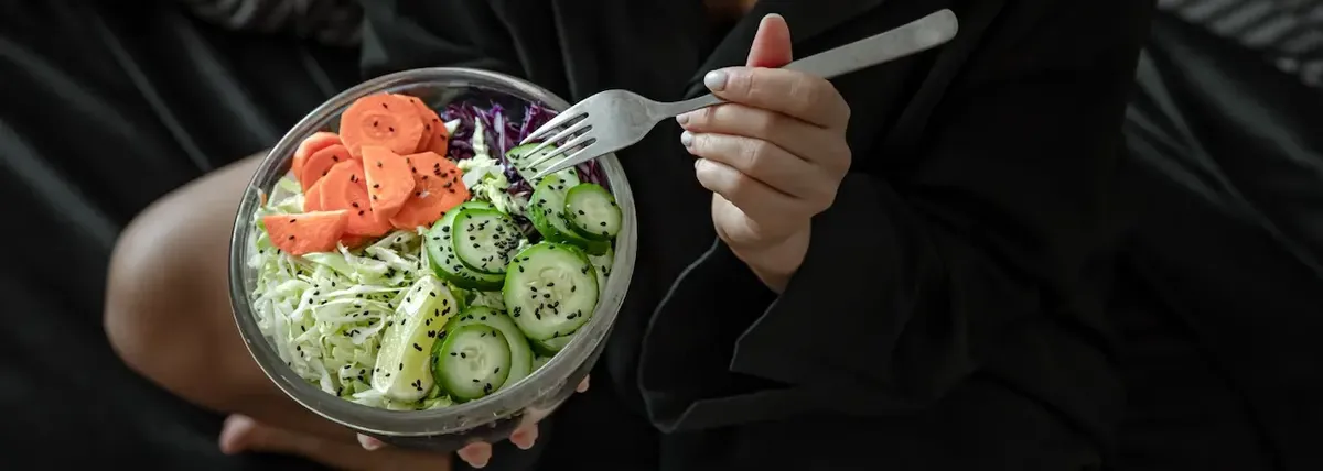  un'insalata in una ciotola di vetro, con carote, cavolo viola, cetriolo e semi neri. L'immagine comunica un senso di benessere e alimentazione sana