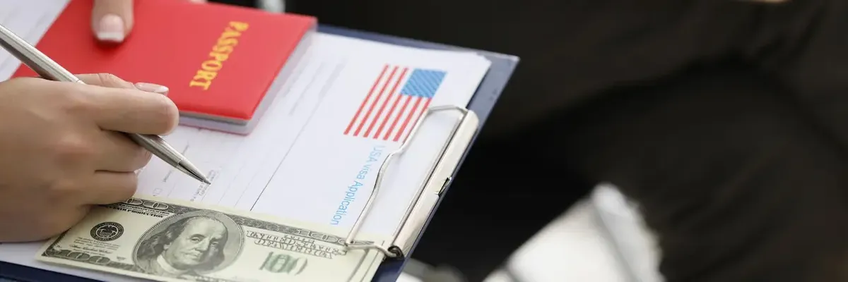 Scena in cui una persona compila un modulo di visto USA con passaporto e banconota da 100 dollari