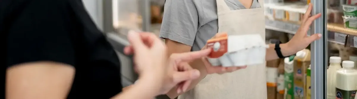 Cliente e addetto in un supermercato davanti al banco frigo, simboleggiando la ricerca di prodotti specifici e l'attenzione di Whole Foods alle richieste dei clienti (Non-OGM)