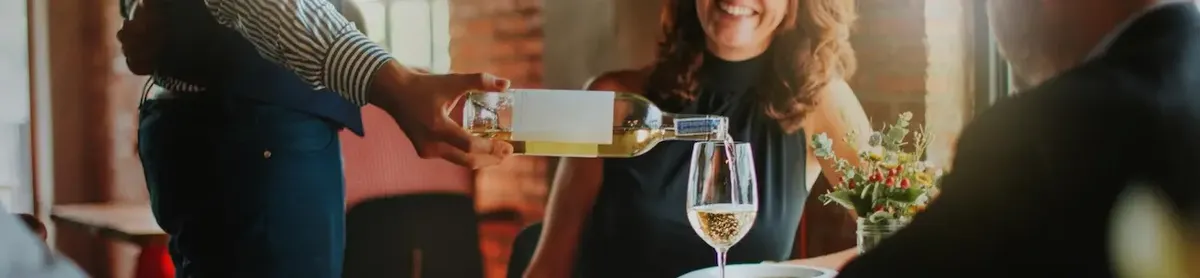 Cameriere versa vino a una cliente in un ambiente raffinato e accogliente di New York, simboleggiando la qualità del servizio e l'esperienza di degustazione